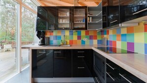 A modern kitchen with black cabinets, a colorful tile backsplash, and a large window overlooking a deck.