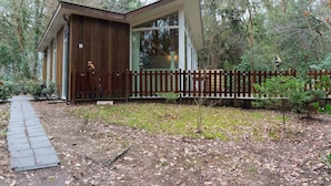A wooden cabin with a sloped roof, a wooden fence, and a paved path leading to the entrance.