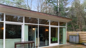 A modern house with large glass doors, a wooden deck, and a dining area visible through the glass.