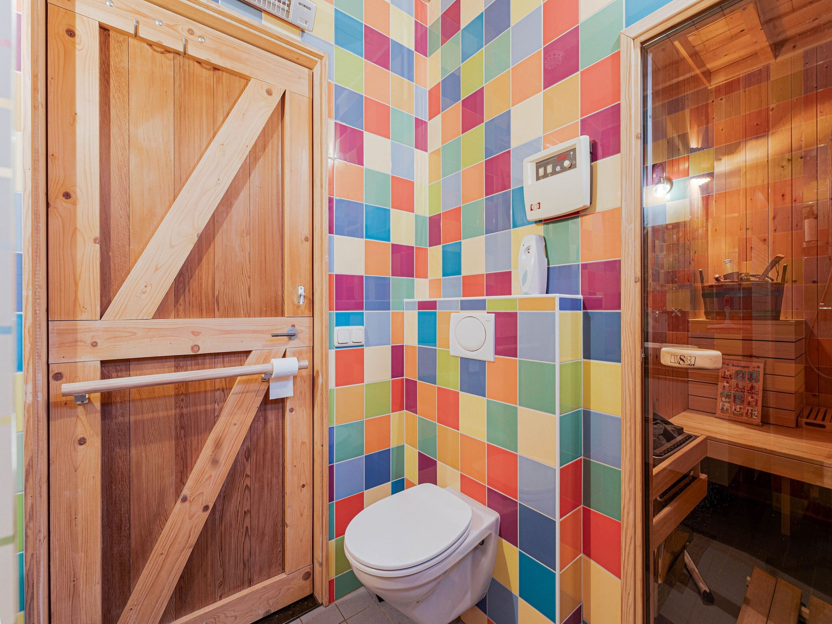 A wooden door, a toilet, and a colorful tiled wall.