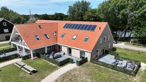 Un edificio moderno con techo de tejas rojas, paneles solares y una zona de estar exterior cubierta.