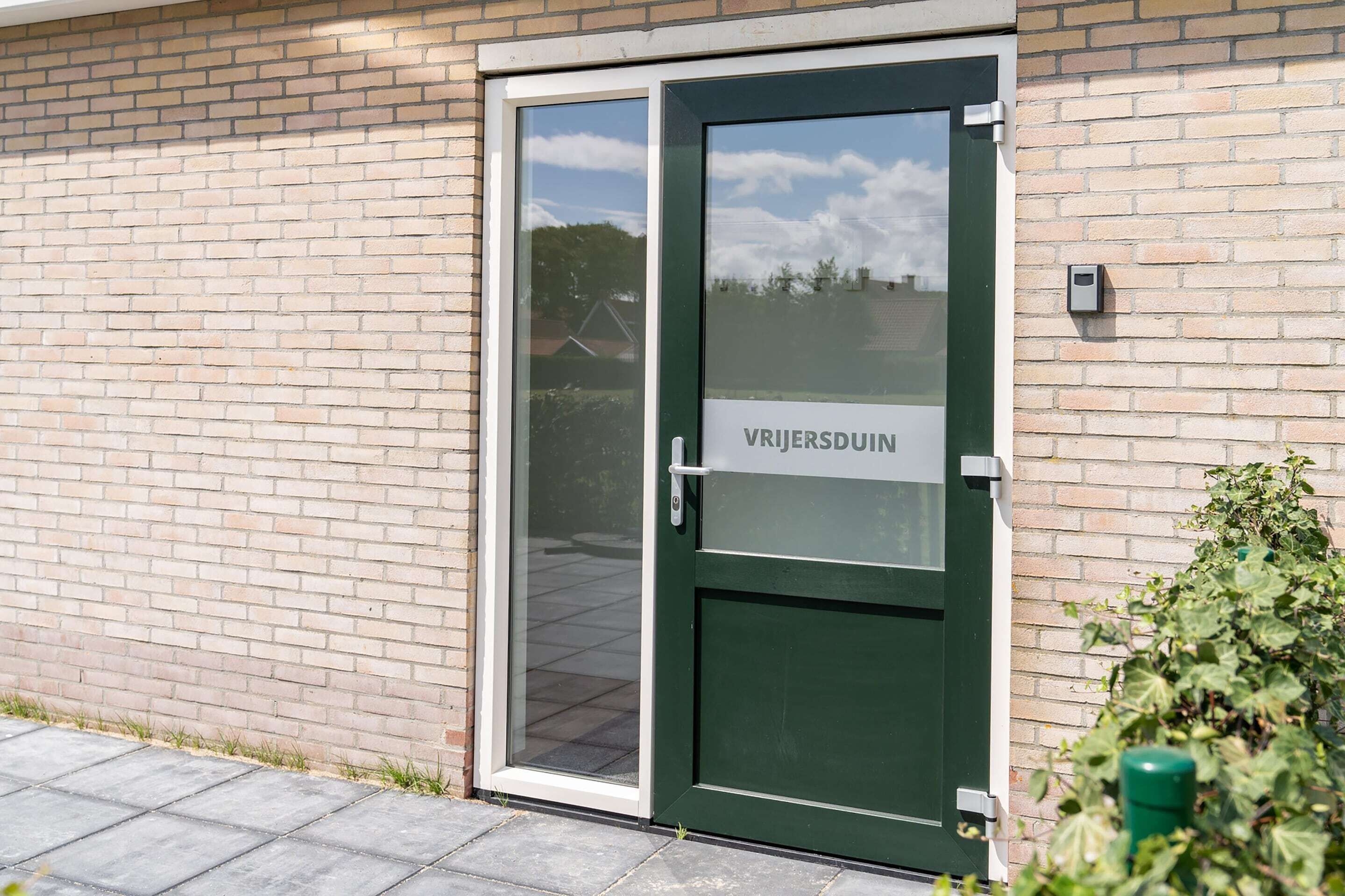 A green door with a sign reading "VRIERSPUIN" on a brick building.