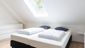 Un dormitorio con dos camas, un tragaluz y una pared blanca.