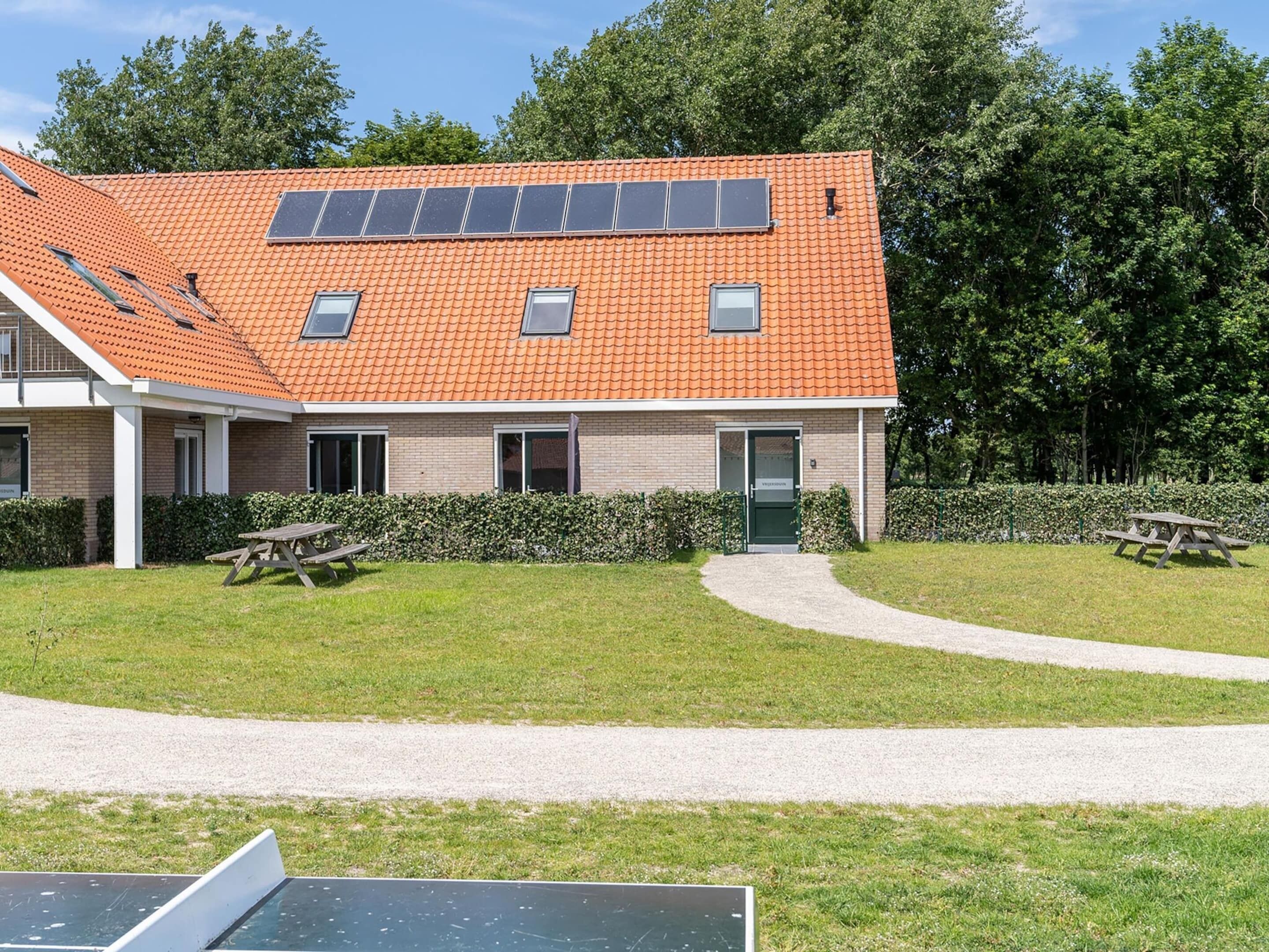 Un bâtiment doté d’un toit recouvert de tuiles, de panneaux solaires et d’un chemin pavé menant à une porte.