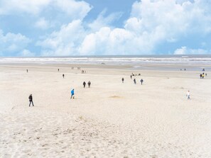 A wide sandy beach with people walking and playing, and the ocean in the background. - Apartment in Nes Near Vlijen Recreation Area (Nes)