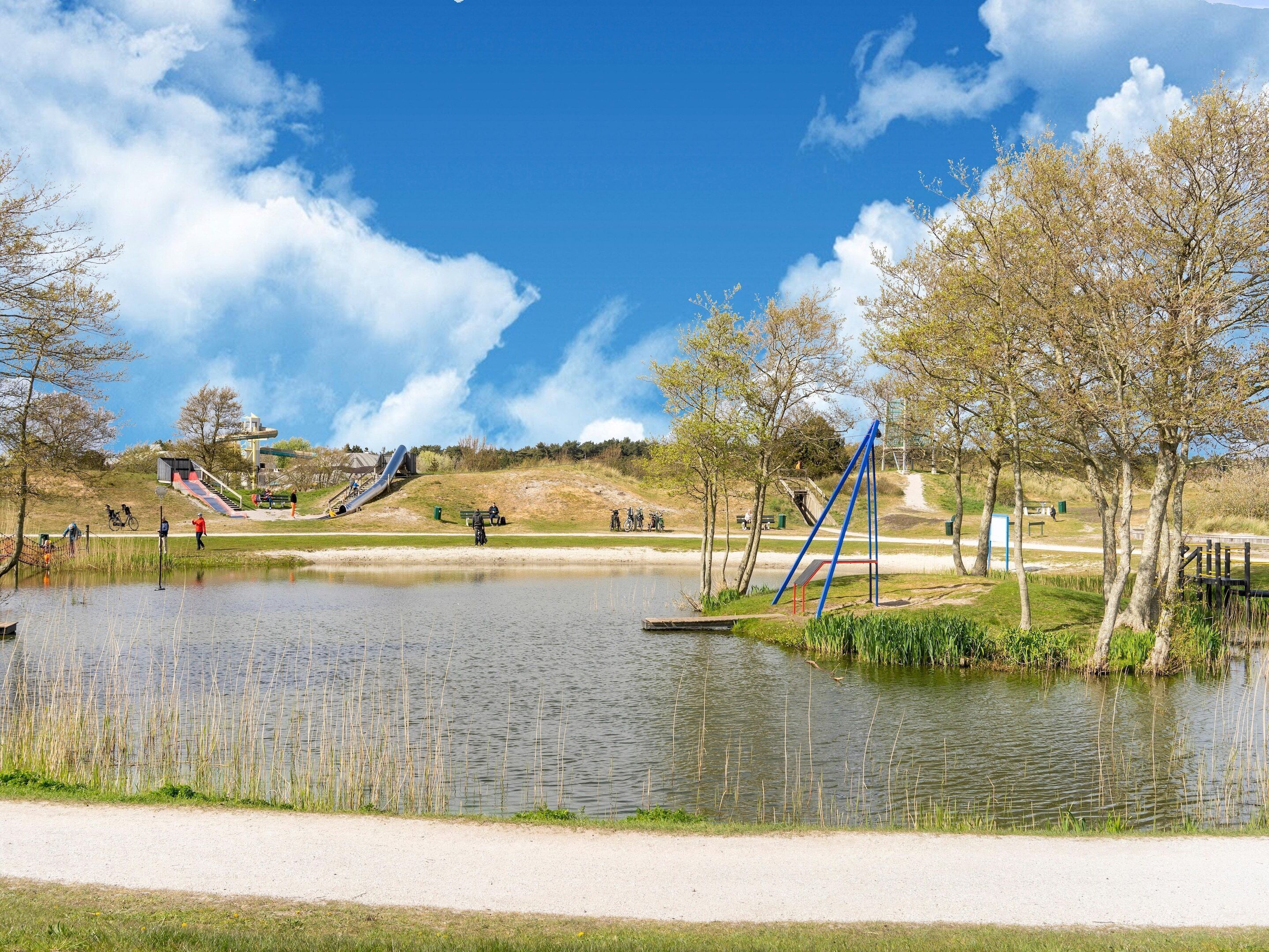 Ein Park mit Teich, Spielgeräten und blauem Himmel.