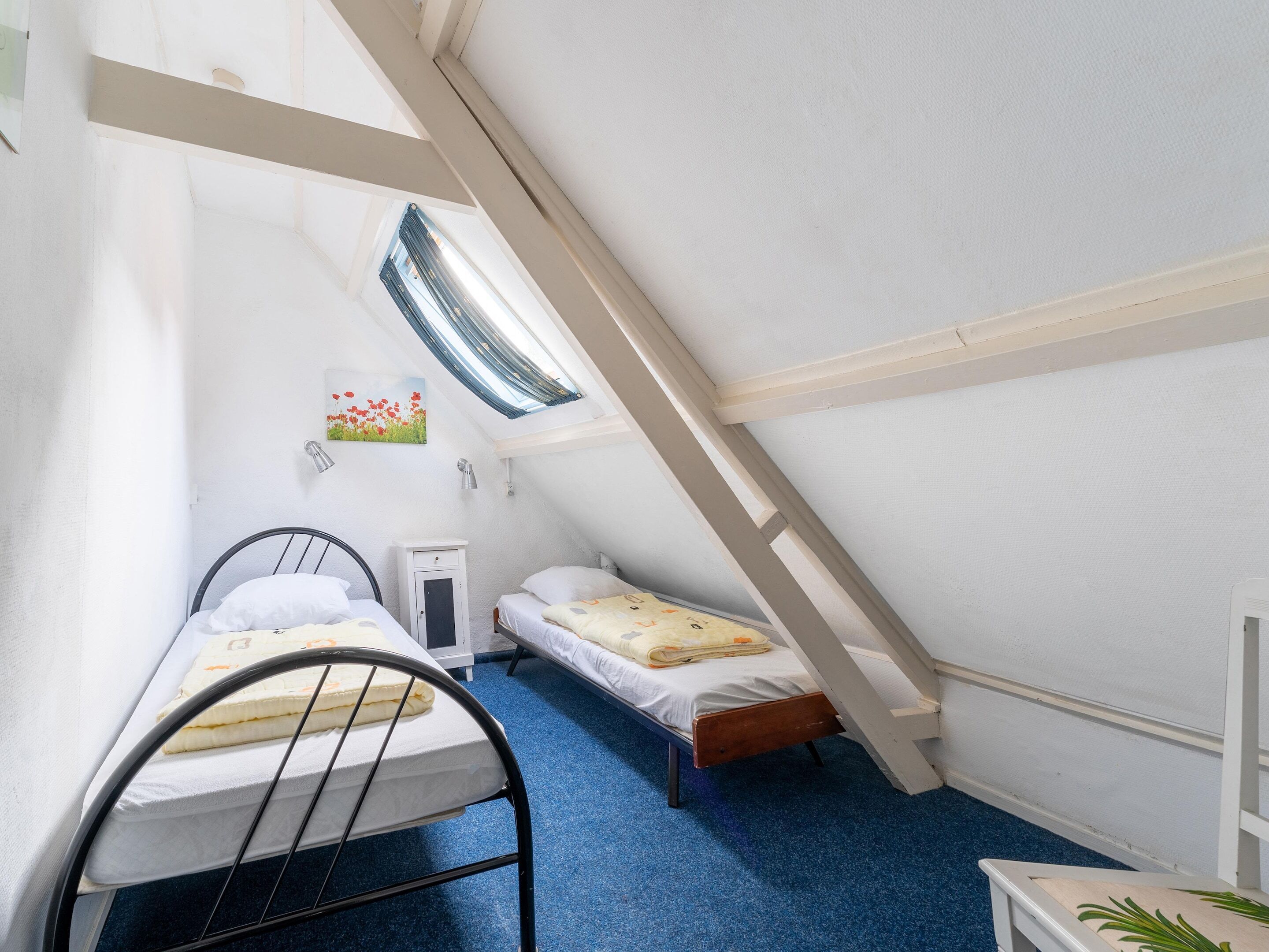 A small, cozy attic bedroom with two single beds, a desk, and a window providing natural light.