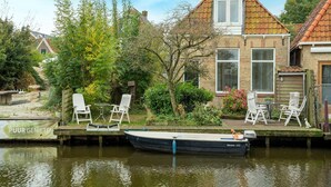 A canal-side house with a boat docked in front, surrounded by greenery and a clear sky. - Waterside Stay With Private Jetty (Heeg)