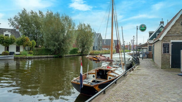A canal with boats docked, a brick building with a sign, and trees in the background. - Waterside Stay With Private Jetty (Heeg)