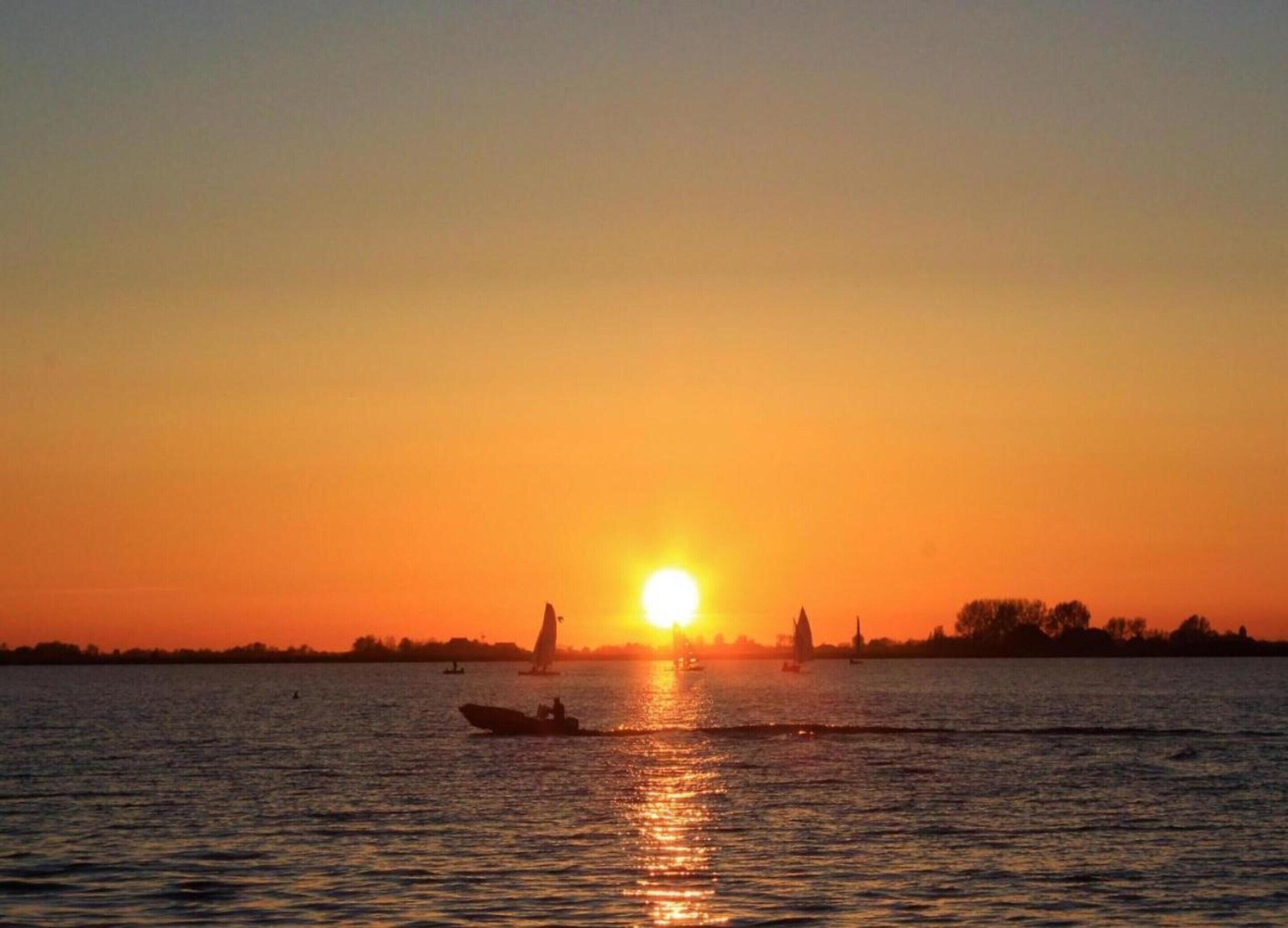 A sunset over a calm body of water with boats and a distant shoreline.
