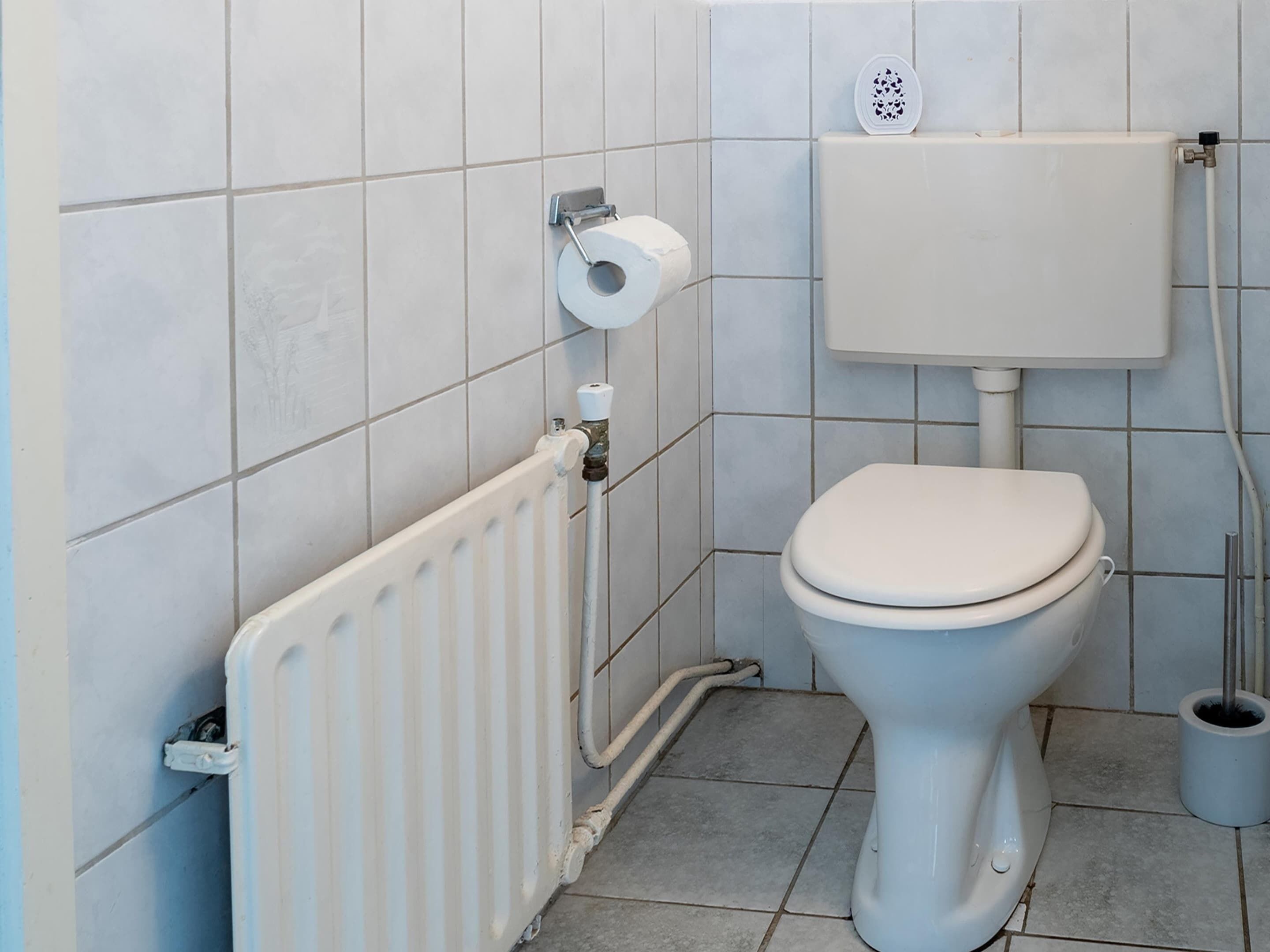 Une petite salle de bain propre, équipée de toilettes, d’un radiateur et d’un porte-rouleau de papier toilette.