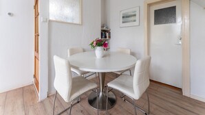 A dining area with a round table, four chairs, a vase with flowers, a bookshelf, and a door with a frosted glass panel. - Waterside Stay With Private Jetty (Heeg)