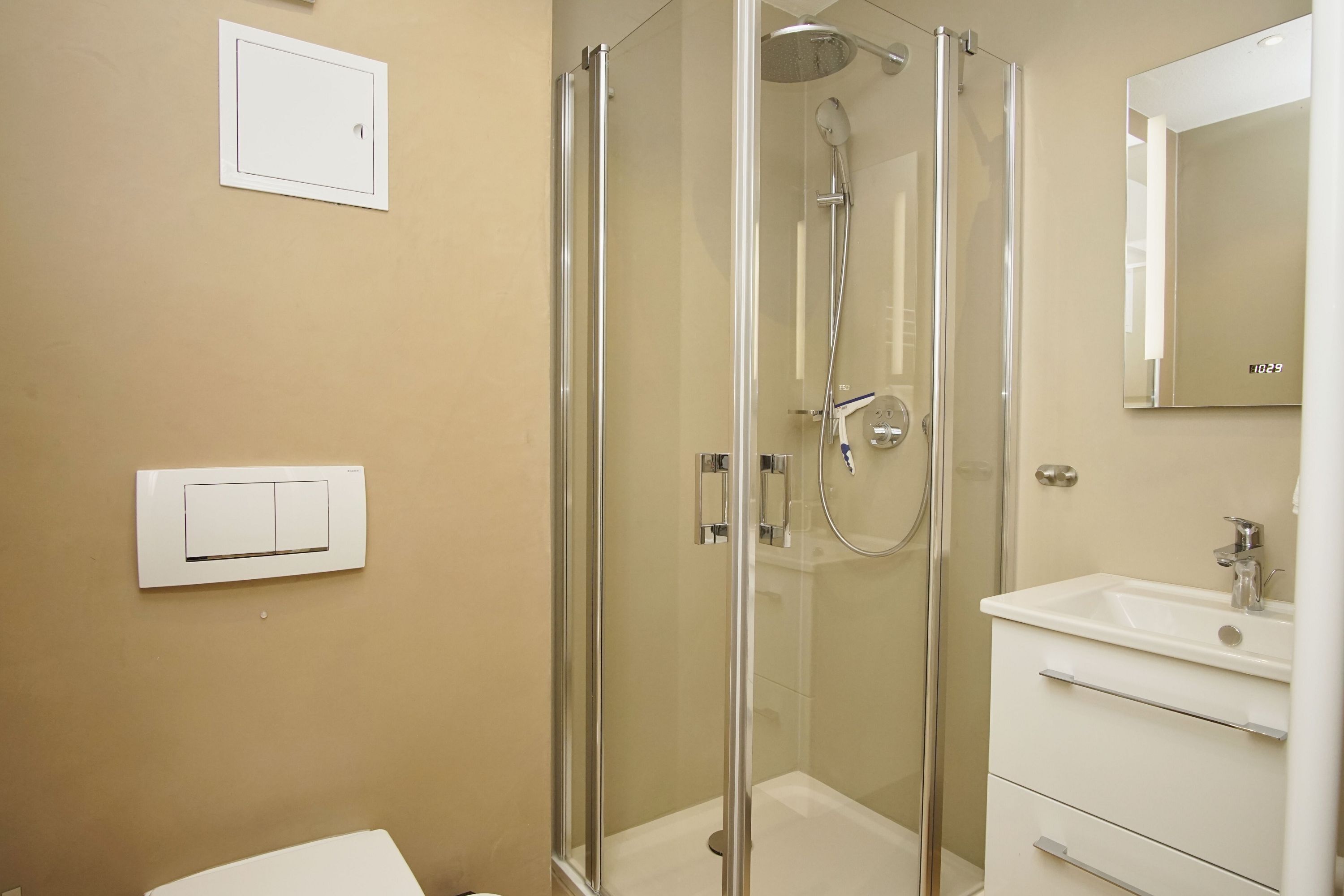 Un baño moderno con ducha de vidrio, un lavamanos blanco y un espejo sobre él.