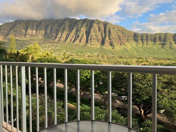 A balcony with a view of a mountainous landscape, lush greenery, and a road with vehicles. - Ocean & Mountain View Studio in a Resort-Like Complex. Makaha Valley, West Oahu (Waianae)