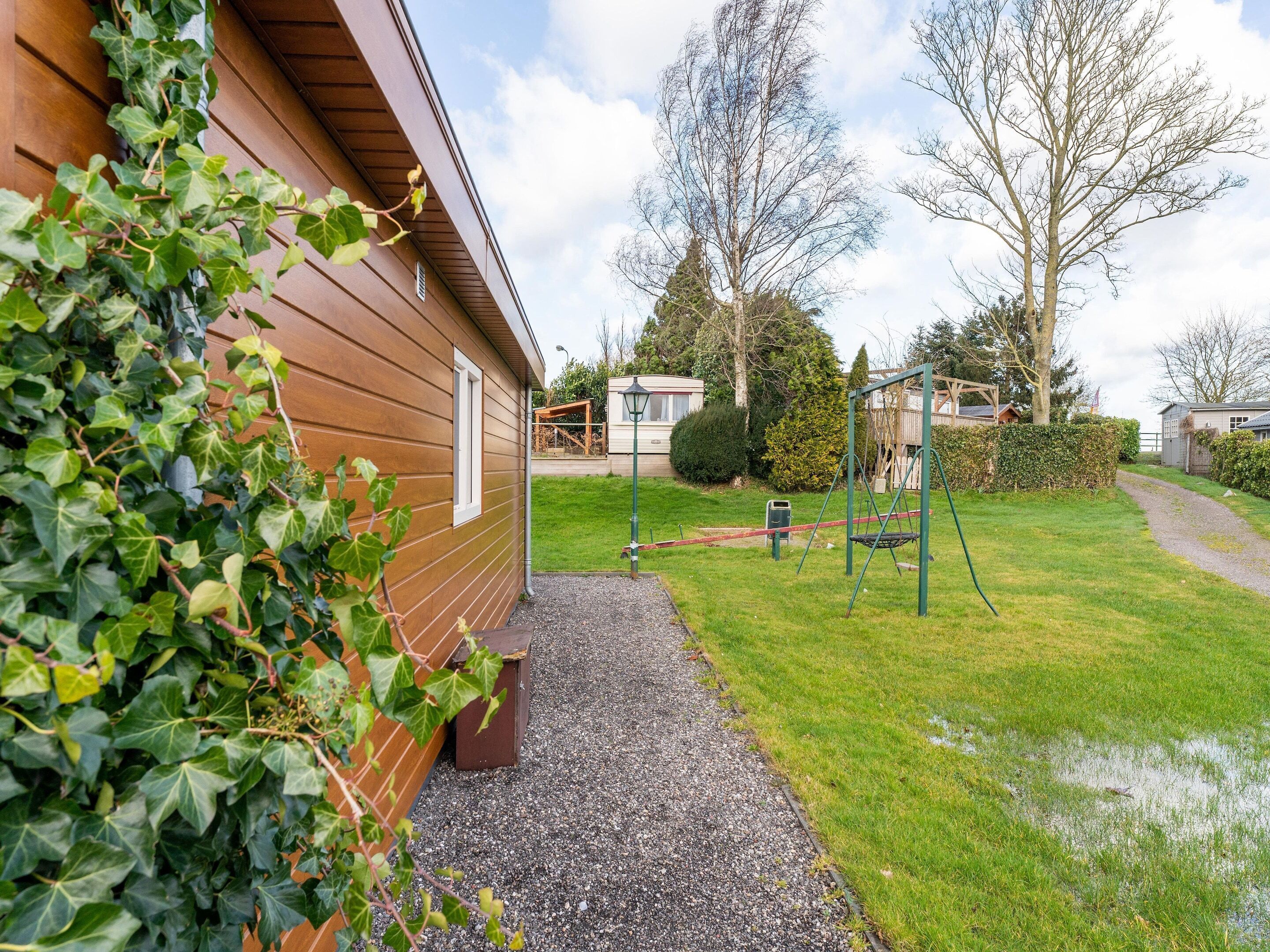 A wooden building with a gravel path leading to a grassy area with a swing set.