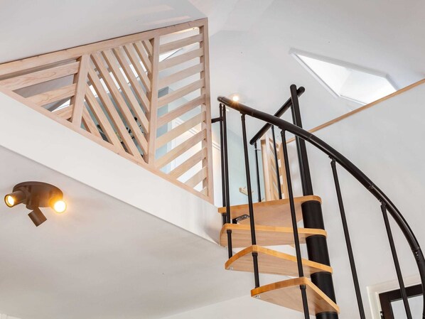 A modern staircase with wooden steps and black metal railings, leading to a lofted area with a slatted wooden partition and skylights.