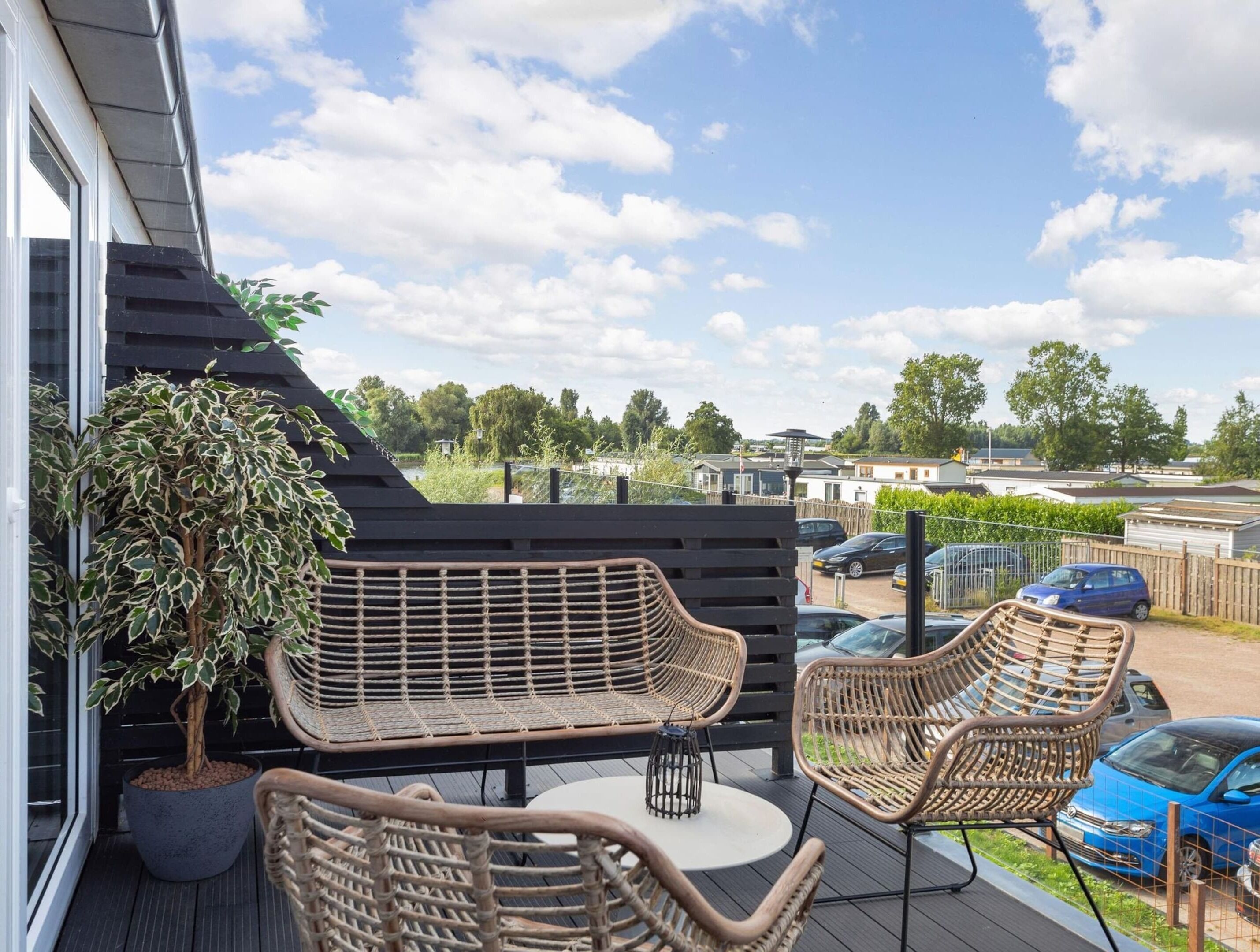 A deck with wicker furniture, a potted plant, and a view of a residential area.