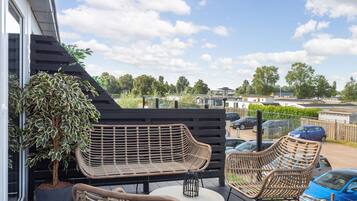 A deck with wicker furniture, a potted plant, and a view of a residential area.