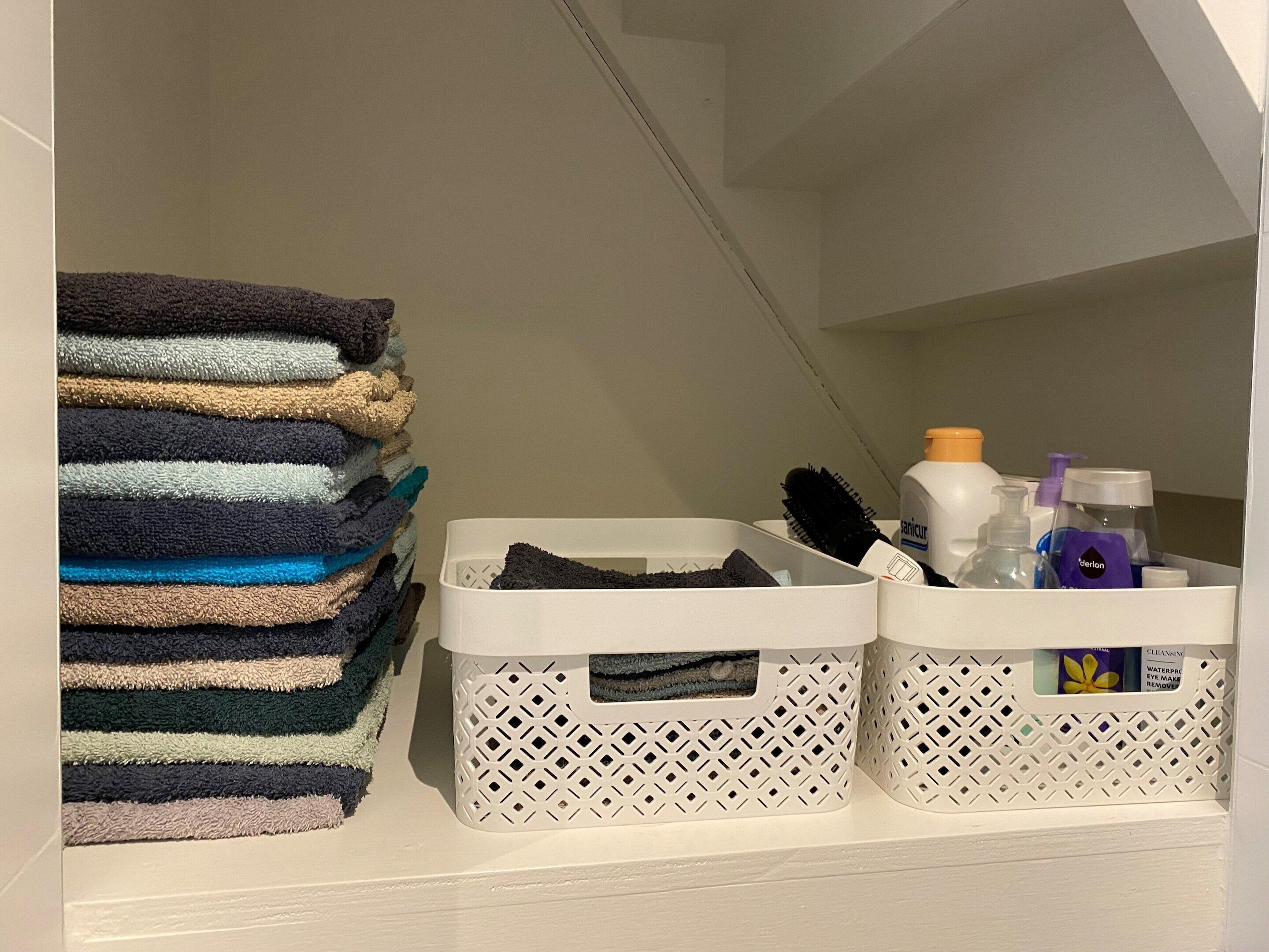 Een keurig opgeruimde wasmand met opgevouwen handdoeken en toiletartikelen.