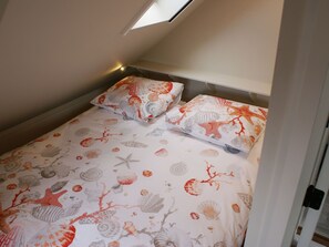 Une petite chambre avec un lit simple, un plafond en pente et un puits de lumière.