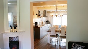 A modern kitchen with white cabinets, a dining area with wooden chairs, a fireplace, and a chandelier. - Holiday Home Paesens Near Wadden Sea (Paesens)