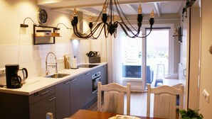 A modern kitchen with a dining area, featuring a chandelier, a coffee maker, and a view of the outdoors. - Holiday Home Paesens Near Wadden Sea (Paesens)