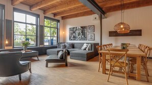 Un salón amplio con un ventanal grande, un sofá gris, una mesa de comedor con sillas de madera y una lámpara colgante.