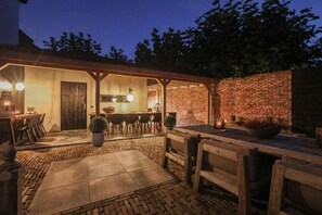 An outdoor patio area with a brick wall, wooden furniture, and a well-lit bar area. - Inn in Ternaard Near Heritage (Ternaard)