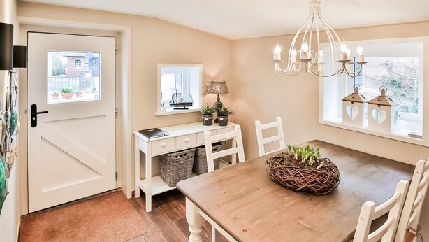 Een eetruimte met een houten tafel, witte stoelen, een kroonluchter en uitzicht door het raam.