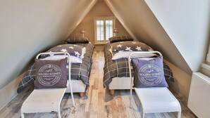 Een kleine, driehoekige slaapkamer op zolder met twee bedden, elk voorzien van beddengoed en kussens met een sterenpatroon.