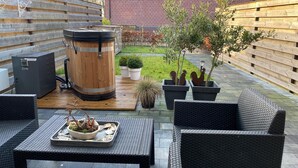 Een terras met rieten meubilair, een houten vat, potplanten en een bakstenen gebouw op de achtergrond.