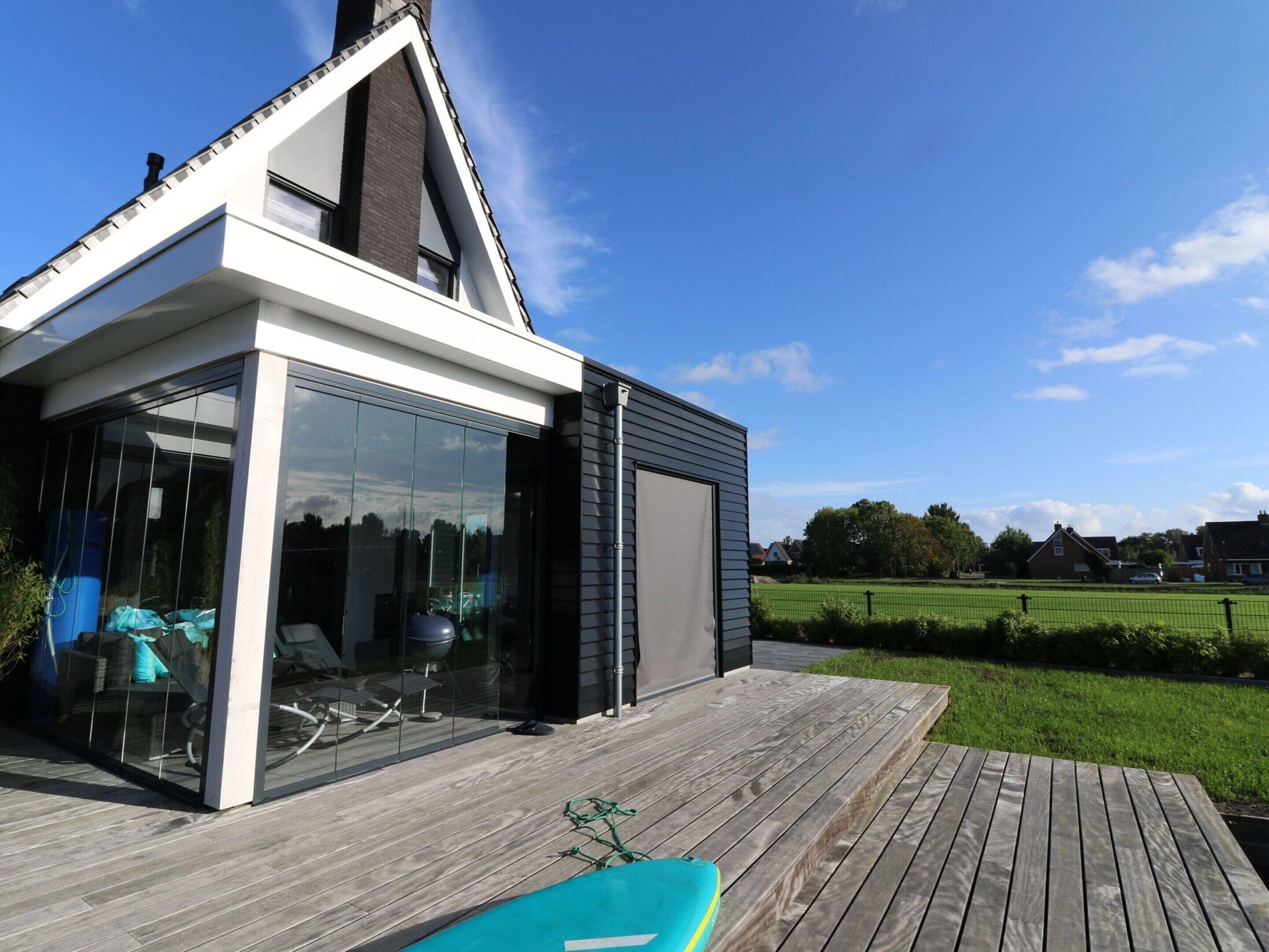 A modern house with a large glass window, a wooden deck, and a swimming pool.