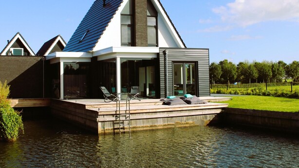 A modern house with a sloped roof, large windows, and a deck extending over a body of water. - Holiday Home in Stavoren by Private Jetty (Stavoren)