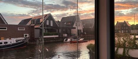 Vista de un canal con barcos, un muelle de madera y casas tradicionales al fondo.