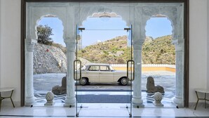 A view through an arched doorway with a beige car parked outside, a stone lion statue, and a clear sky. - Fateh Vilas by Fateh Collection (Udaipur)