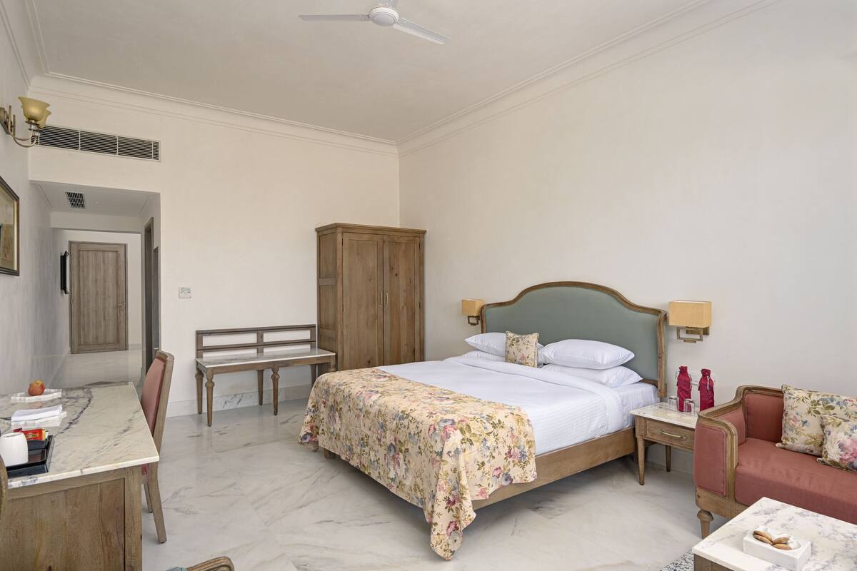 A bedroom with a bed, a desk, a chair, a wardrobe, and a nightstand with lamps.