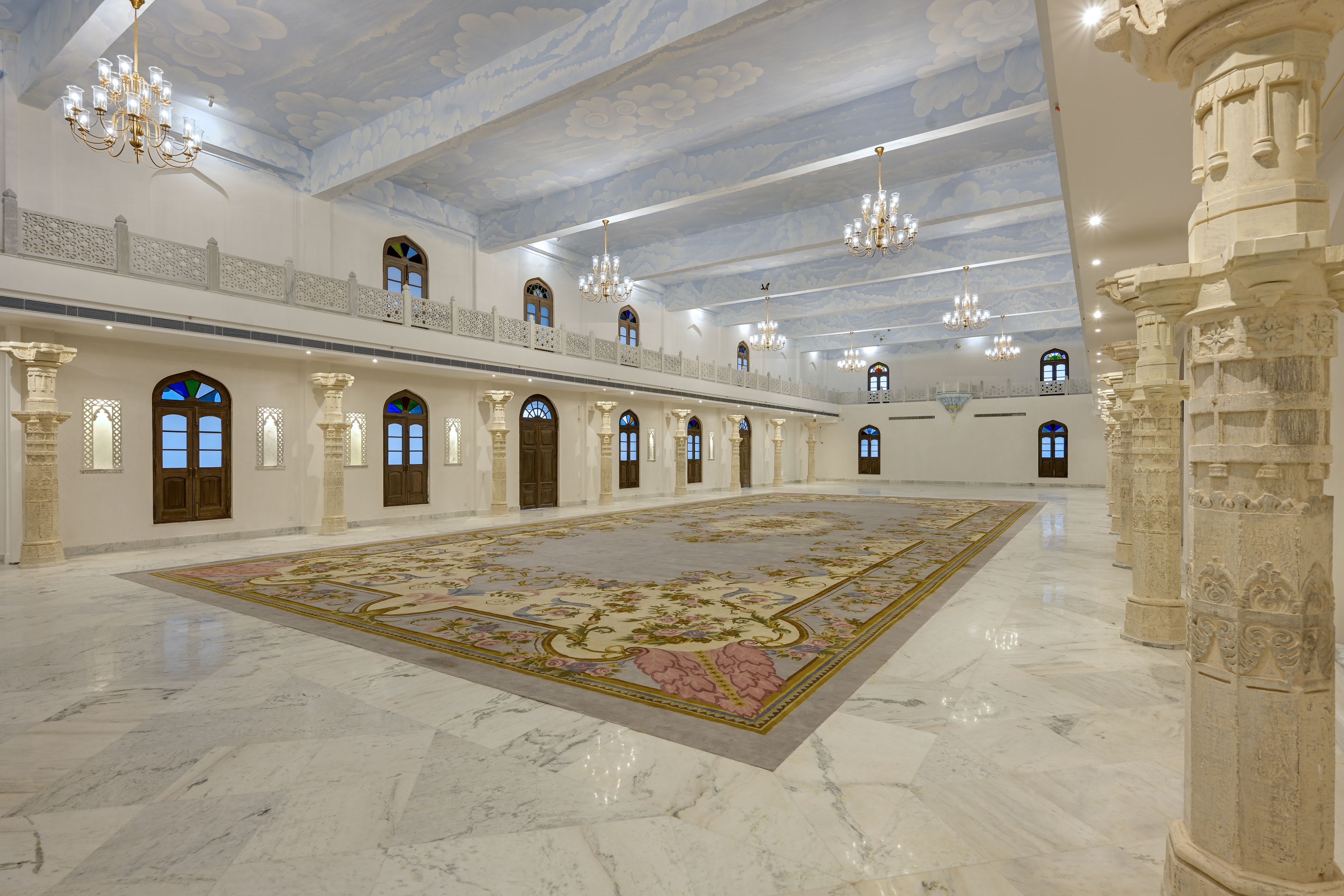 Un amplio salón con un gran alfombra, candelabros y arquitectura clásica.