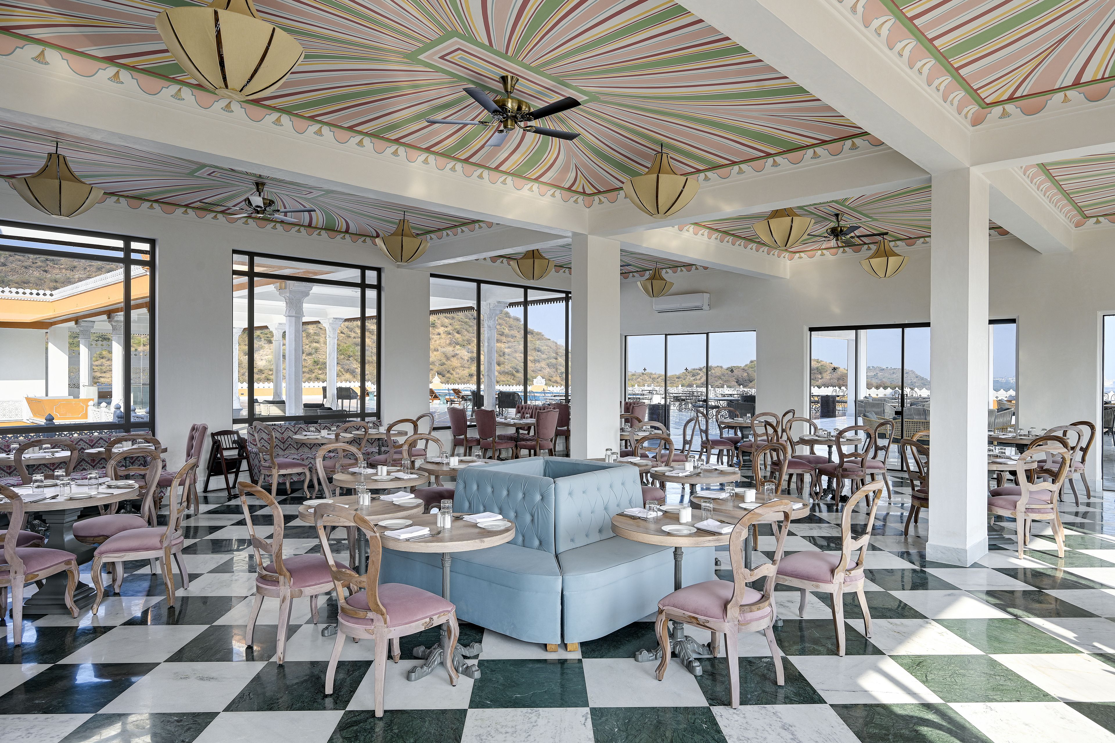 A spacious dining area with checkered flooring, multiple tables and chairs, and large windows offering a view of the landscape.