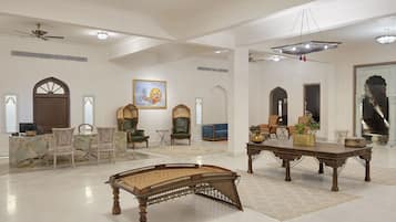 A spacious room with a large wooden bench, a dining area with chairs, a painting on the wall, and a chandelier.