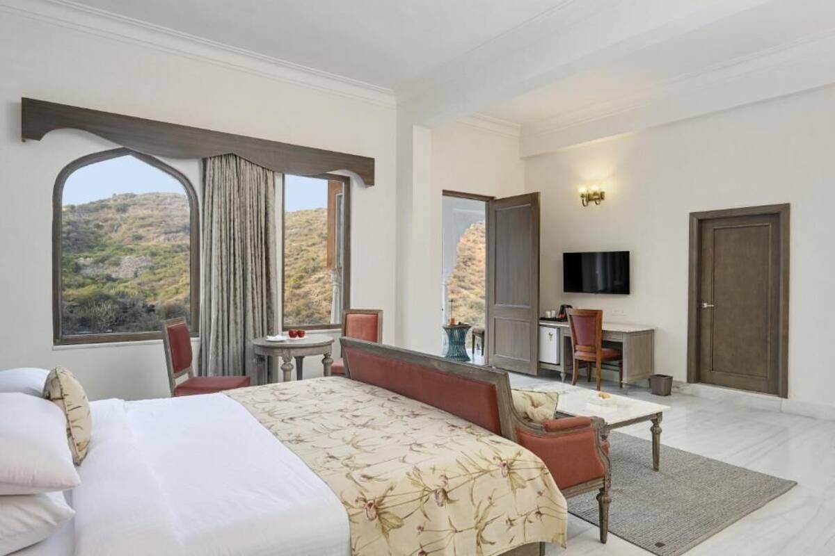 A hotel room with a bed, a desk, a chair, a TV, and a view of the outdoors.
