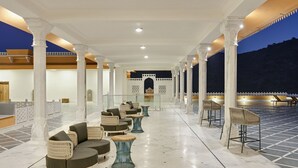 A covered outdoor seating area with sofas and tables, white columns, and a view of a mountainous landscape at dusk. - Fateh Vilas by Fateh Collection (Udaipur)