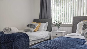Ein Hotelzimmer mit zwei Betten, weißer Bettwäsche, einem Nachttisch mit einer Vase und einem Fenster mit Jalousien.