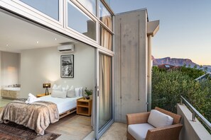 Un dormitorio moderno con una cama grande, una mesita de noche, una lámpara y vistas a las montañas.
