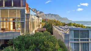 Ein modernes Gebäude mit großen Fenstern, einem Balkon und Blick auf den Ozean und die Berge.