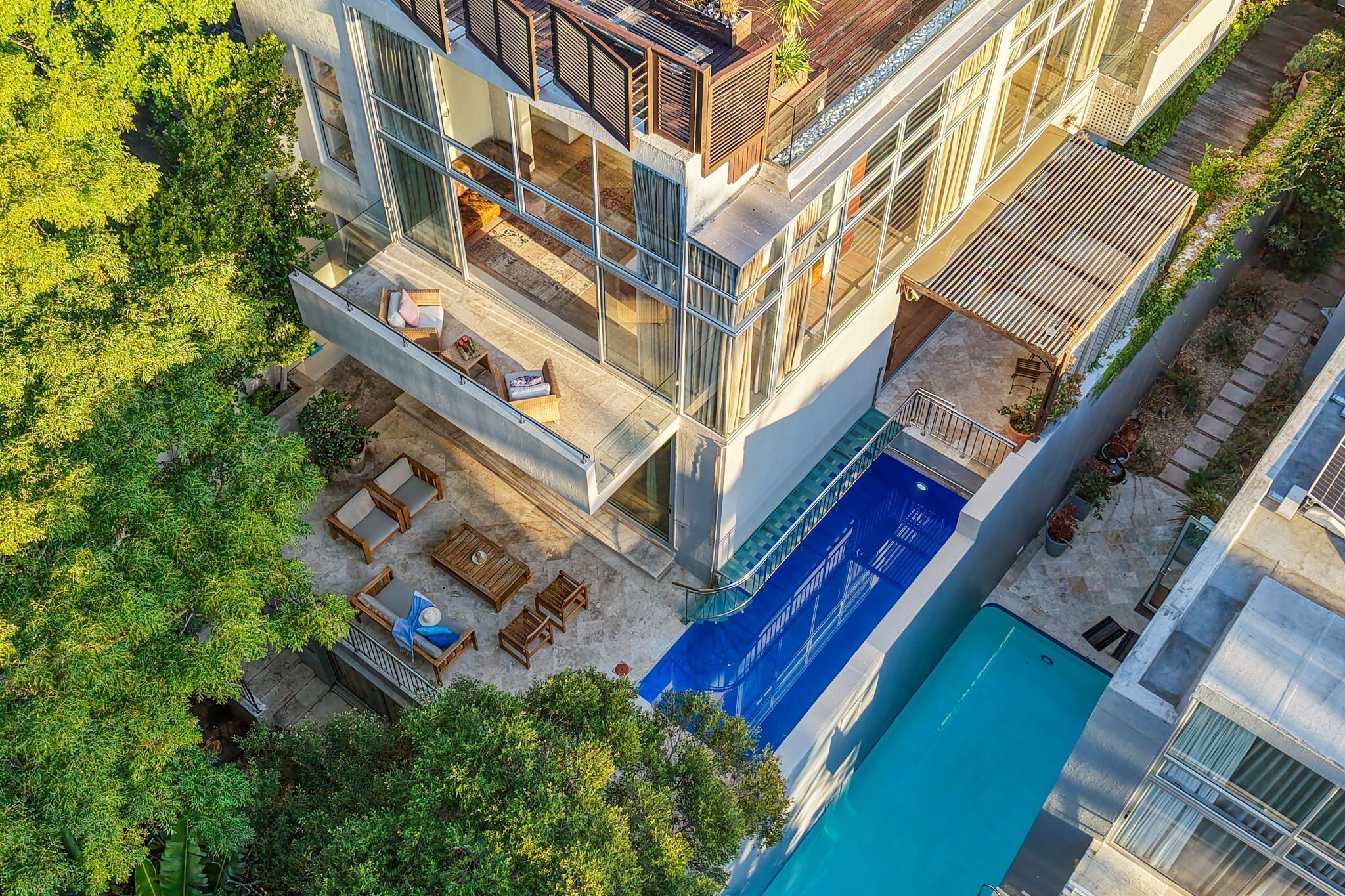 A modern multi-story building with a rooftop deck, a swimming pool, and lush greenery surrounding the property.
