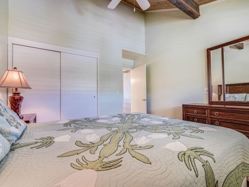 A bedroom with a floral bedspread, a wooden dresser, a mirror, and a lamp.