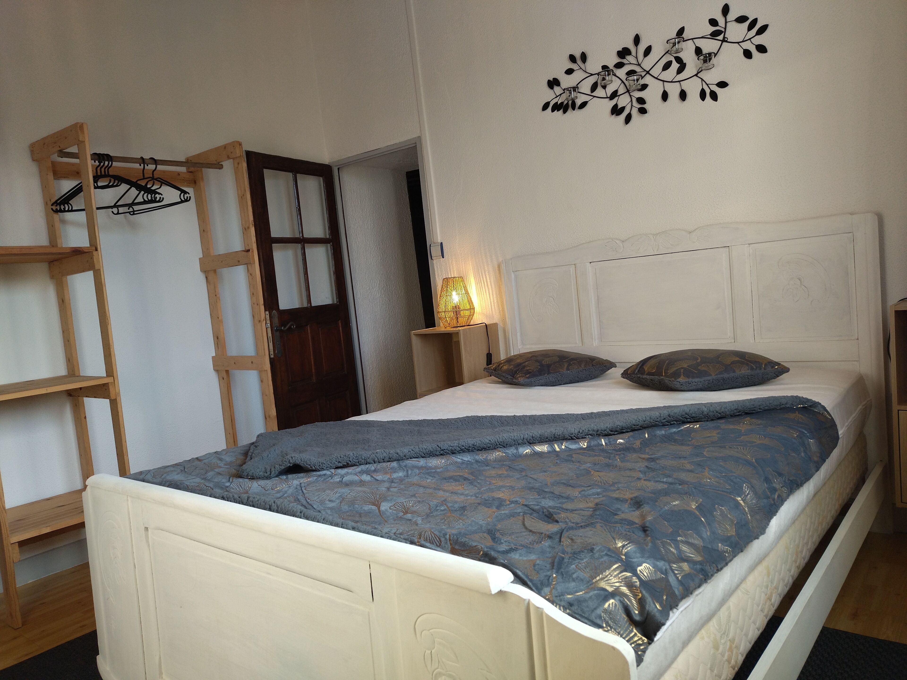 A bedroom with a bed, wooden ladder, and a wall-mounted light fixture.