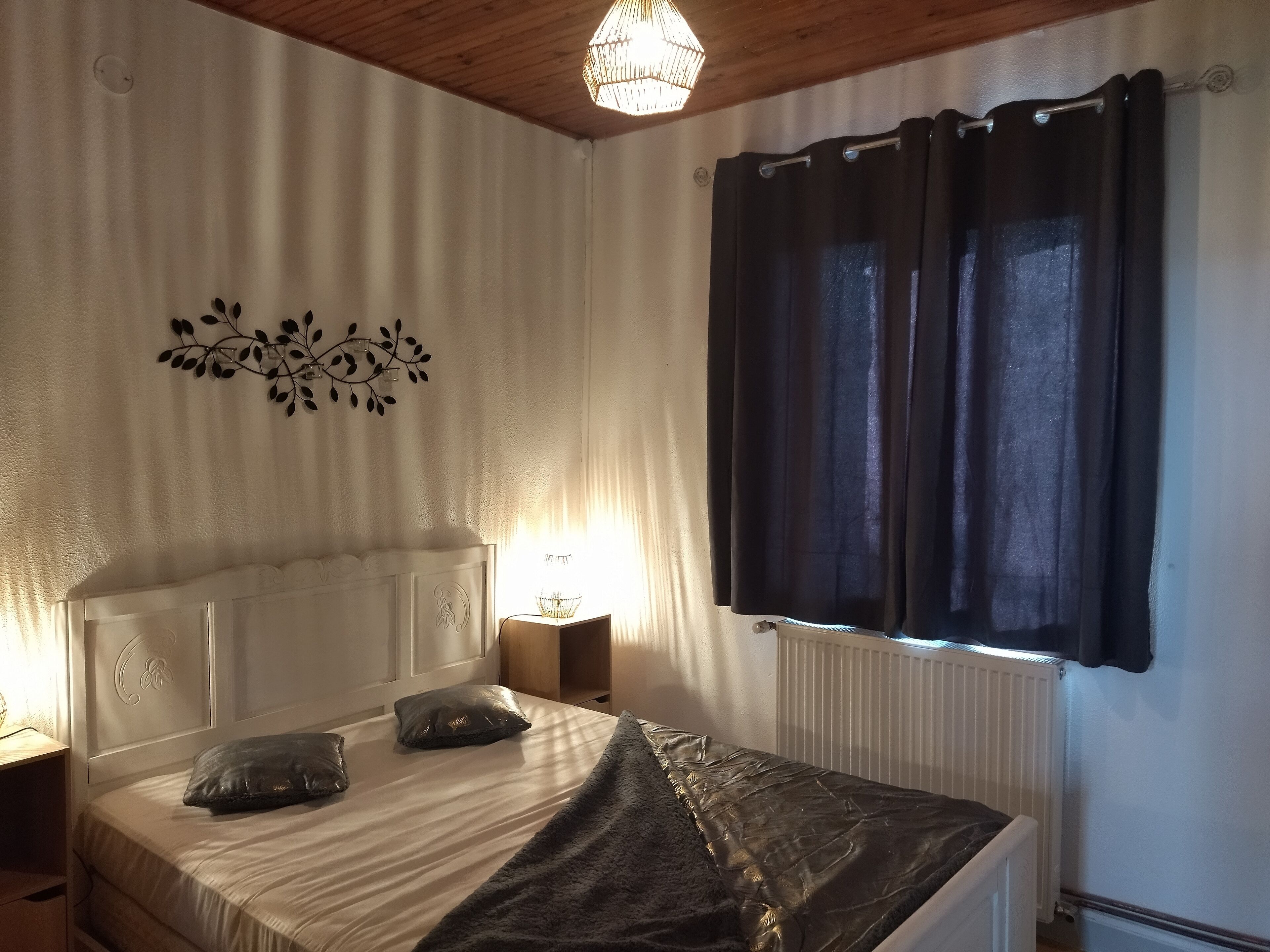 Een slaapkamer met een bed, nachtkastje, lamp en raam met gordijnen.