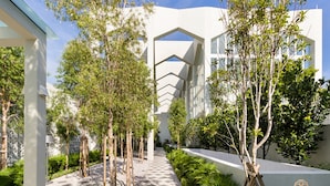 Ein modernes Gebäude mit einer geometrischen Fassade, umgeben von einem angelegten Garten mit Bäumen und einem Schachbrettmuster-Weg.