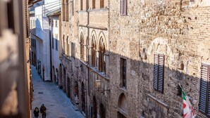 A narrow street with historic buildings, a flag, and a few pedestrians. - [Old Town] Elegant Suite, Wi-fi & Comfort (San Gimignano)